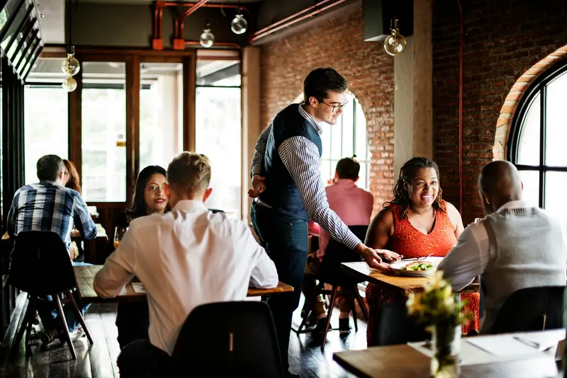 Guests at their tables in a restaurant while a waiter serves, three of them tagged Nut allergy, VIP and First visit